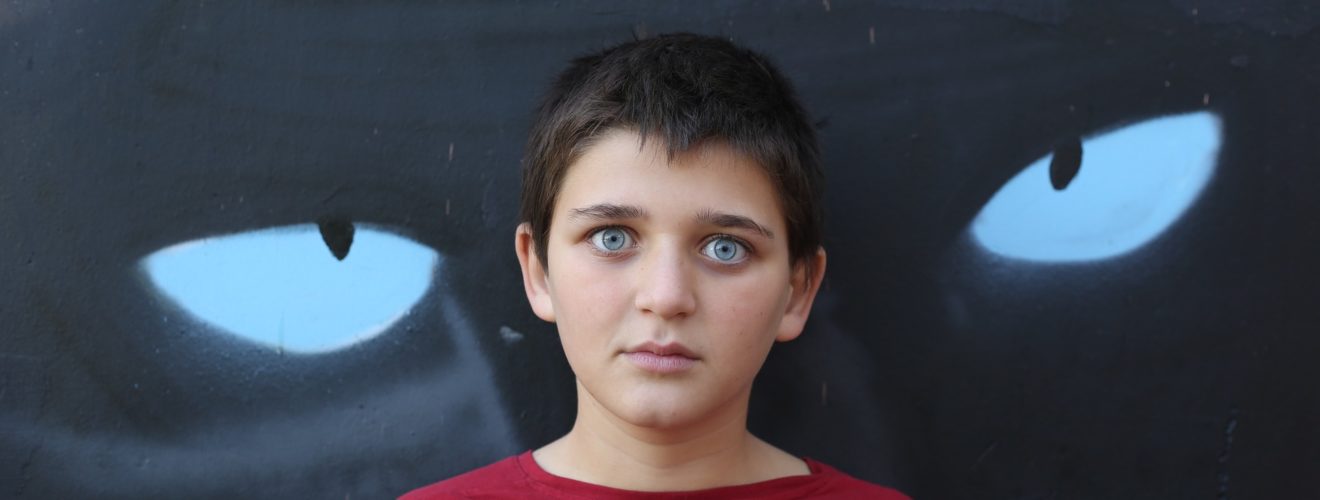 Scared child standing in front of a wall with cat eyes graffiti