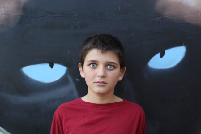 Scared child standing in front of a wall with cat eyes graffiti